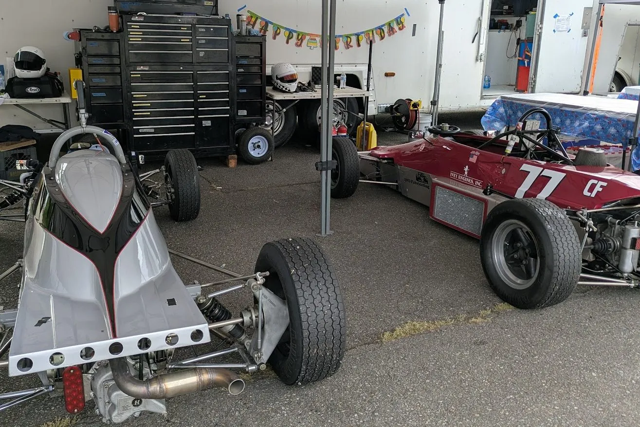 The tail of the number 3 car beside a red number 77 under a paddock tent