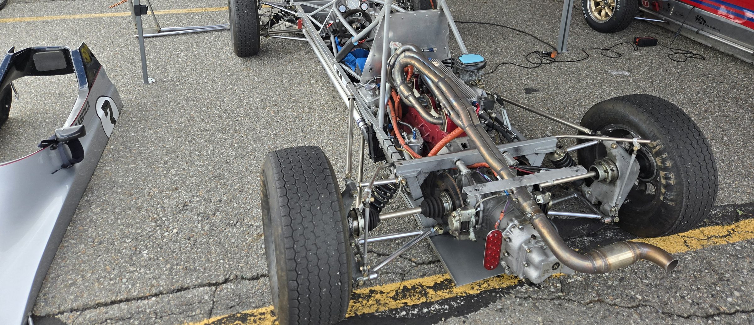 The car with its bodywork removed, showing the tube-frame chassis, engine, exhaust, and rear suspension
